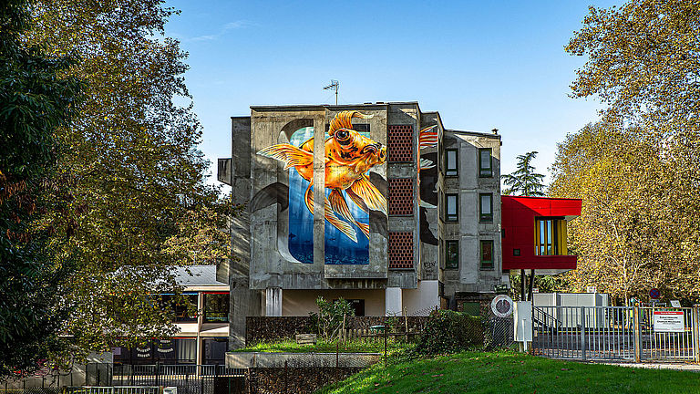 Au milieu d'arbres lesimmeubles d'une résidence. Sur l'une des façades, un poisson japonais est représenté sur toutes la hauteur.